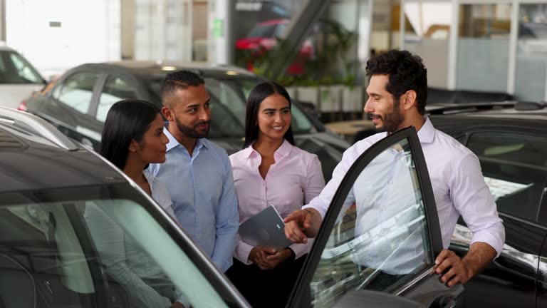 Handsome male manager explaining the new features of a car at the dealership to his team talking very cheerfully while they all pay attention