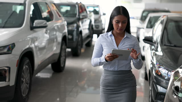 Beautiful saleswoman checking the retail display versus a list on digital tablet at the car showroom