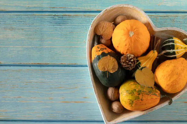 Decorative pumpkins, nuts, and autumn leaves in heart-shaped bowl placed on wooden background, Top table view, copy space. Fall harvest season, love for plant-based food, thanksgiving concept.