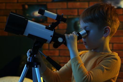 Little boy looking at stars through telescope in room