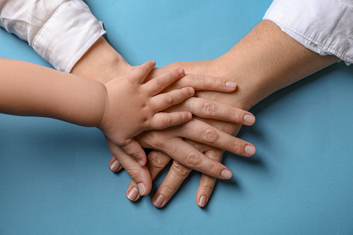Family holding hands together on light blue background, top view