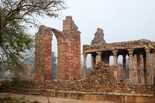 This image features the Qutub Minar, one of Delhi's most iconic landmarks, shrouded in the soft haze of an early morning. Standing at a height of 73 metres, the Qutub Minar is the tallest brick minaret in the world and is known for its intricate carvings and inscriptions. The haze adds an ethereal quality to the photograph, slightly obscuring the minaret's details but enhancing its mystique. This atmospheric condition offers a different perspective on a well-known monument, adding a layer of complexity and mood. The image aims to capture both the historical significance and the natural surroundings of the Qutub Minar, presenting it as a must-see attraction with ever-changing moods and appearances.