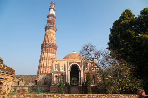 This image features the Qutub Minar, one of Delhi's most iconic landmarks, shrouded in the soft haze of an early morning. Standing at a height of 73 metres, the Qutub Minar is the tallest brick minaret in the world and is known for its intricate carvings and inscriptions. The haze adds an ethereal quality to the photograph, slightly obscuring the minaret's details but enhancing its mystique. This atmospheric condition offers a different perspective on a well-known monument, adding a layer of complexity and mood. The image aims to capture both the historical significance and the natural surroundings of the Qutub Minar, presenting it as a must-see attraction with ever-changing moods and appearances.