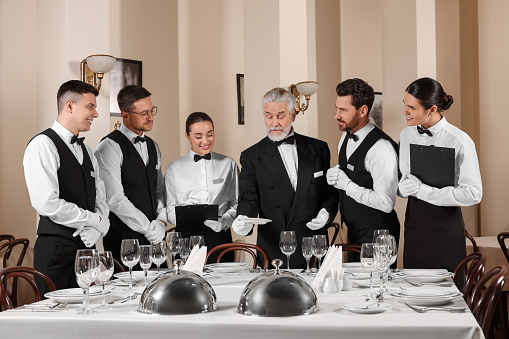 Senior man wearing formal suit teaching trainees in restaurant. Professional butler courses