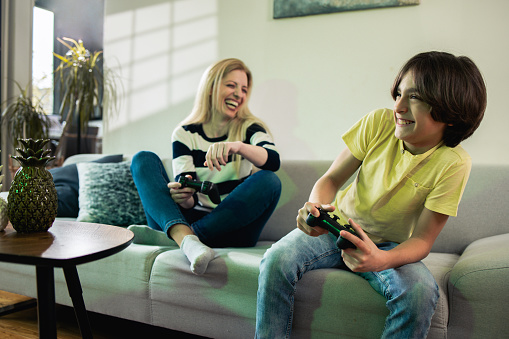 Woman and her son playing video games at home and having fun