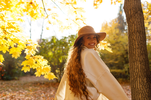 Smiling young woman enjoys the autumn weather in the forest with the yellow leaves at evening time