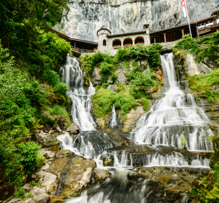 Waterfalls flow beneath the monastery located on the side of a cliff near the entrance of St. Beatus Caves near Lake Thun, Switzerland
