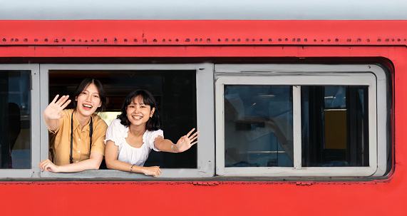 Two young asian female traveler waving hand from train window.