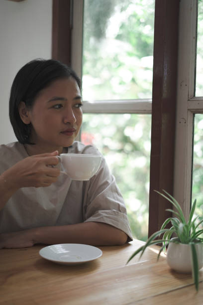 istock woman sitting drinking coffee next to the window 1743788437