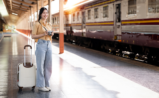 Young female traveler standing at train station with a  suitcase