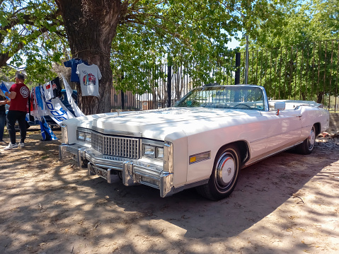Remedios de Escalada, Argentina - Oct 8, 2023: Old luxury white 1976 Cadillac Eldorado convertible two door in a park under the trees. Classic car show. Copyspace