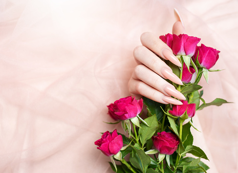 Elegant pastel pink natural manicure. Female hands  with roses on pink silk background.