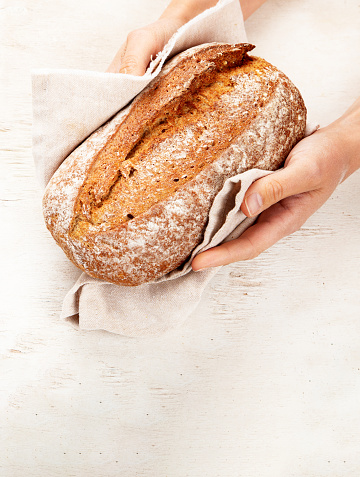 Baker or cooking chef holding fresh baked bread in hands on a light background. Concept of cooking.