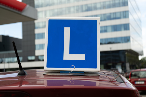 Driving school car roof sign. Vehicle rooftop blue learner plate with letter L. Student driver class, learning how to drive. Taking lessons with instructor to pass the driver's license exam in Poland.