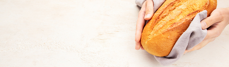 Baker or cooking chef holding fresh baked bread in hands on a light background. Concept of cooking. Panorama.