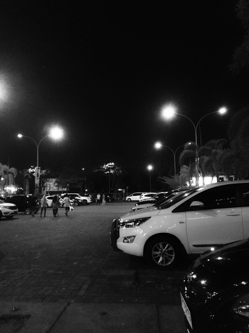 Lombok, Indonesia - 14 October 2023:
row of cars in outdoor uncovered parking lots in modern shopping center at night. Black and white tone with noise effect
