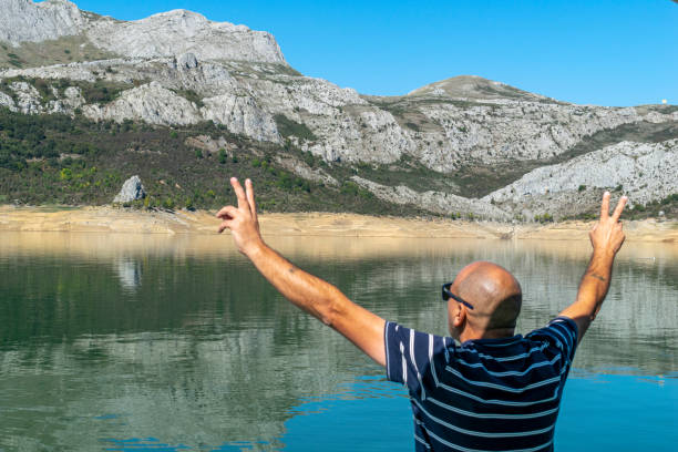 un hombre de mediana edad estira los brazos mientras contempla un embalse de alta montaña. - travel destinations mountain hiking profile fotografías e imágenes de stock