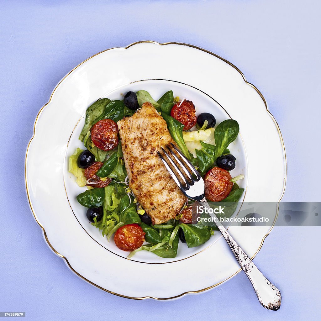 Fresh salad with baby spinach, chicken and black olives A fresh salad made with baby spinach, grilled chicken breast, black olives, and cherry tomatos set on a vintage white plate with golden edging. All placed on light blue background. Appetizer Stock Photo