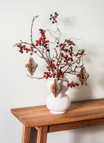 Christmas bouquet on a wooden table. Cranberry Branches with paper craft Christmas toys in a ceramic vase