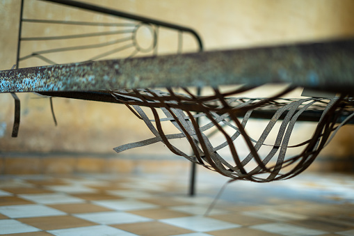 A poignant stock image capturing the grim remnants of an abandoned, decaying prison cell. The focus of the photograph is an old, rusty bed with ominous leg shackles attached, serving as a haunting reminder of the harsh and inhumane conditions that once prevailed within the prison's walls.\n\nIn this image, the rusted metal, peeling paint, and dimly lit surroundings create an atmosphere of desolation and despair. The leg shackles are a chilling testament to the suffering and confinement experienced by inmates in years past.\n\nThis image is a powerful visual representation of the haunting history and stark reality of former prisons, serving as a valuable asset for projects that aim to shed light on the historical significance and the dark legacy of such facilities.