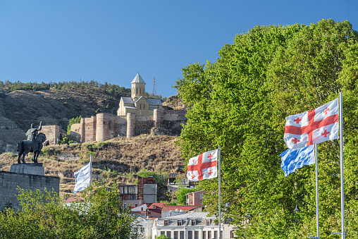 Scenic view of the Saint Nicholas church at Narikala fortress in Old Town of Tbilisi, Georgia. The flag of Georgia is fluttering in wind. Georgia is a popular tourist destination.