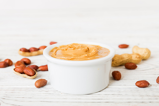 Bowl of peanut butter and peanuts on table background. top view with copy space. Creamy peanut pasta in small bowl.