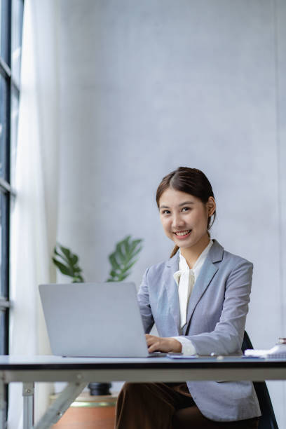 istock Young Asian accountant working in financial office, managing sales reports using calculator with laptop, preparing reports, calculating balances, documents, tax audit. vertical picture 1743951127