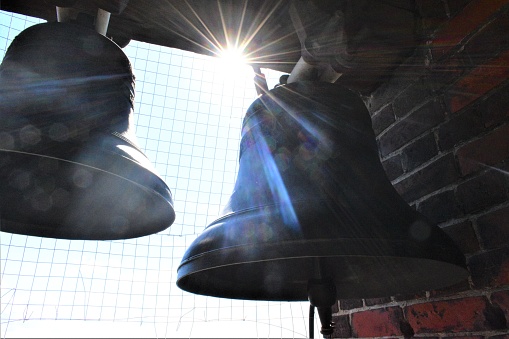 Large church bells on the bell tower. Sunlight between the bells.