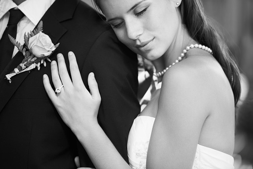 Black and white image of a beautiful bride embracing her husband from behind lovingly