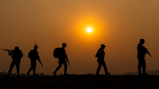 silhouette group of special forces sodiers walking and holding gun over the sunset and colorful orange sky background, special warfare training operations teams,
