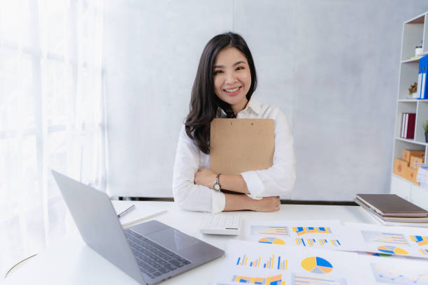 istock Young Asian accountant working in financial office, managing sales reports using calculator with laptop, preparing reports, calculating balances, documents, tax audit. vertical picture 1743975965