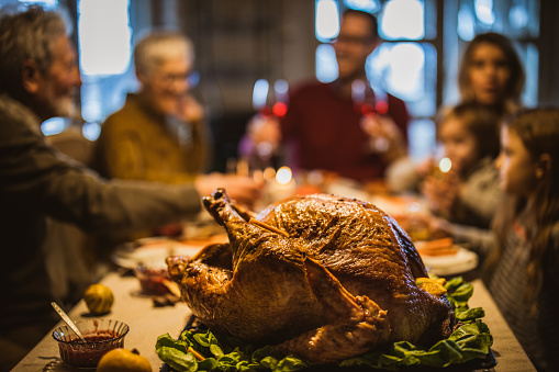 Close up of Thanksgiving stuffed turkey on dining table with family in the background.
