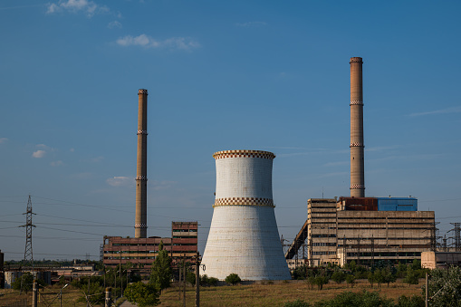 Old, run down and decommissioned power plant with large chimney and smoke stacks, set in a large field in eastern Europe. Late summer daylight, no people.