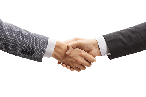 Close up of Businessmen shaking hands. Both are dressed in casual clothing and one is holding a digital tablet with graphs and charts. The  other man is smiling. Shot through a window. There is also a laptop computer on the table