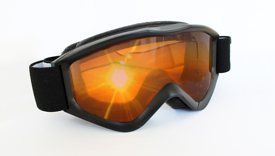 Collage of a trendy cool black ski goggles with the reflection of a beautiful yellow orange red sunset, sunrise, sundawn with sunbeam and sun rays in front of a bright Background with copy space for text