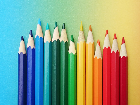 colorful pens arranged in the colors of the rainbow on colorful paper in the course of the rainbow in daylight. the glossy multicolored pencils are made of Wood