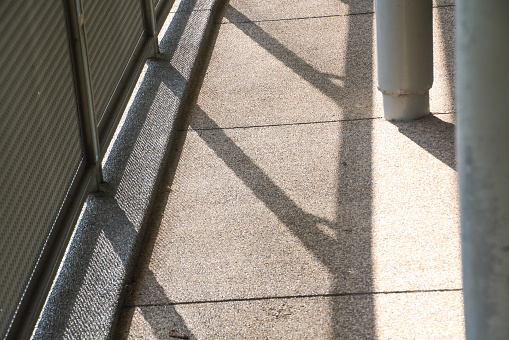 The walkway's shadows, cast by the sun, create an abstract play of light and dark in the outdoor space during the daytime