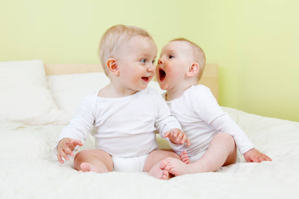 Two babies sitting on bed. One shouting in the other's ear.