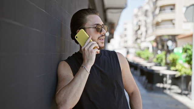 Young hispanic man wearing sunglasses talking on smartphone at street