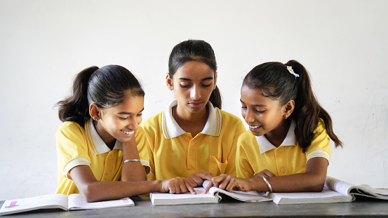 Happy Indian elementary school girls students sitting at desk in classroom with writing in notebook with pencil, Examination and test, female Education concept.