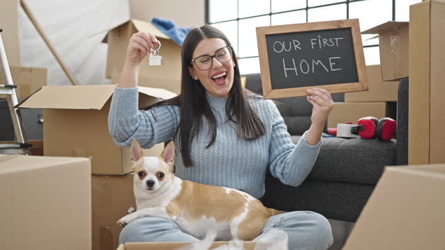 Young hispanic woman with chihuahua dog smiling confident holding blackboard and keys at new home
