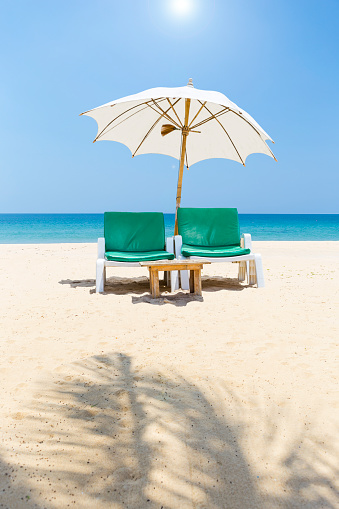 Beach chair under white umbrella on peaceful clean sandy beach, tropical island in south of Thailand, summer outdoor day light, relaxing by the sea, outdoor furniture