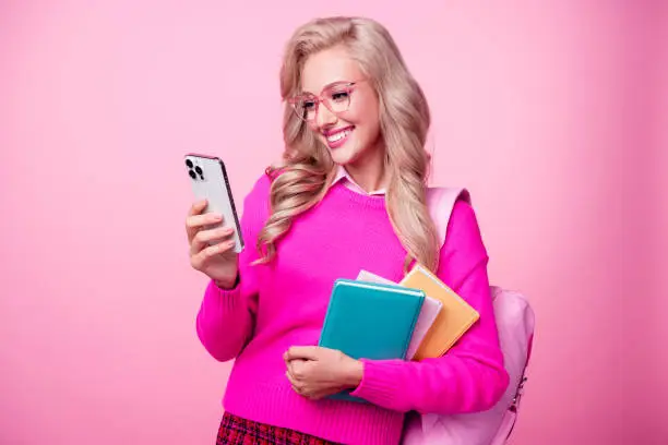 Photo of pretty positive girl wavy hairstyle wear stylish jumper backpack writing sms comment post isolated on pink color background.