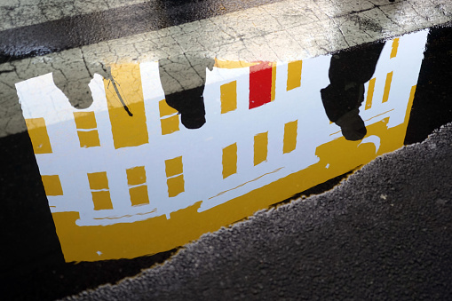 Yellow road markings and red reflected light on wet asphalt surface on city centre street.