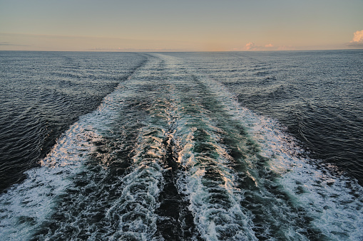 Rear view from cruise ship over the empty sea with trail of waves and white foam created by the ship's engines before sunrise. Holiday and journey concept