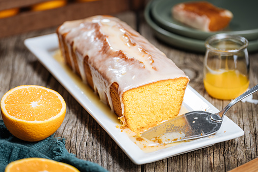 Loaf of sponge dessert called Pound cake with white glazing, served with oranges on rustic wooden background