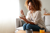 Young relaxed pensive African American woman eating healthy breakfast sitting on the couch. Copy space.