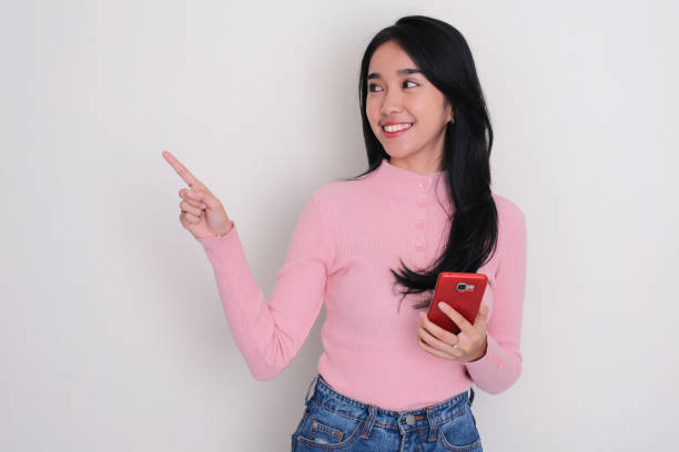 istock A woman looking and pointing to the right side with happy expression while holding mobile phone 1744210648