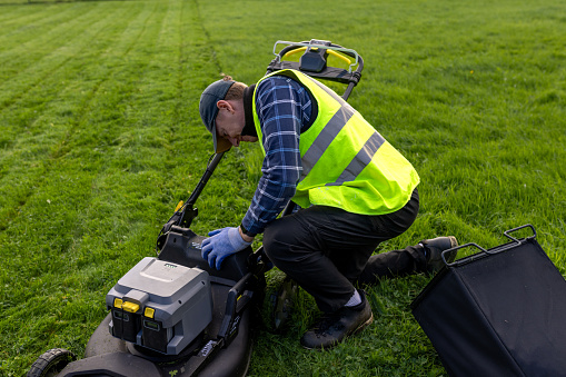 High-angle view full shot of a volunteer at a dog shelter located in Newcastle Upon Tyne. He is emptying a lawnmower of its grass.