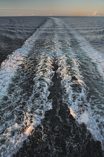 View from aft deck of the cruise ship over empty sea, wake water waves and white foam created by the ship's propellers. Morning sunrise sky. Summer vacation and travel journey concept North sea Norway